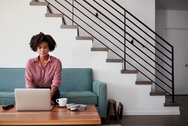Un afro-américain est une femme assise sur un canapé turquoise et à l'aide d'un ordinateur portable